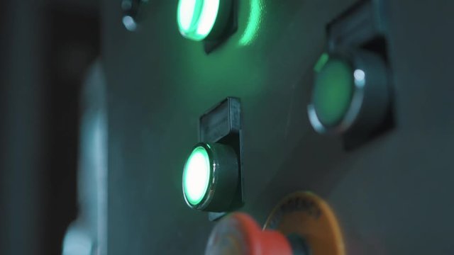Worker hand finger in blue rubber glove push big button that lights up green on manufactory metal control panel, close up
