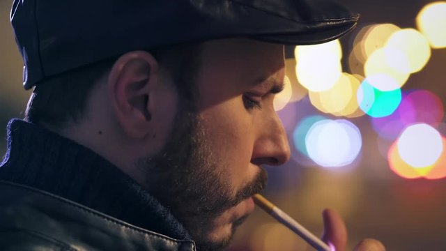Man alone and thoughtful lights a cigarette at night in town, close up