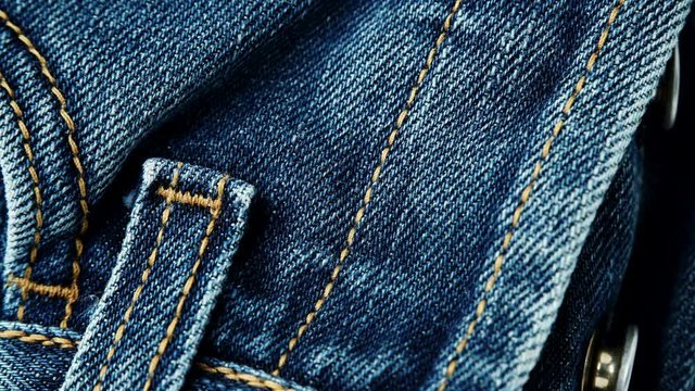 Closeup detail of blue denim jeans front view button zip, belt loop and pocket, texture background. Dolly sliding shot 4K ProRes HQ codec