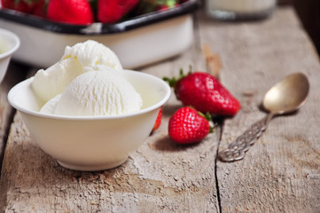 Vanilla ice-cream in a white small bowl with fresh ripe strawberries on a wooden background. Rustic style and close up. Summer food concept.