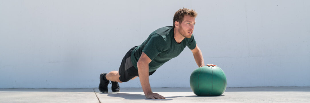 Fitness Man Banner Crop. Athlete Strength Training Pushup Chest And Shoulder Muscles Doing Alternating Single Arm Medicine Ball Push-ups Floor Exercises At Outdoor Gym.