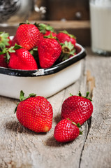 Heap of fresh ripe raw strawberries in a bowl and glass of milk on a wooden background. Rustic style and close up.