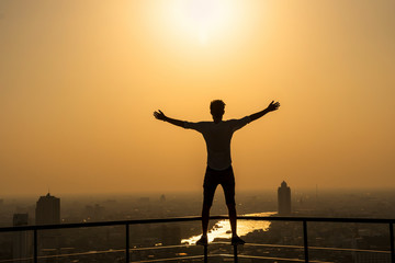 Silhouette of man standing with extend arms action over the cityscape background at sunset time with lens flare,Lifestyle and freedom concept