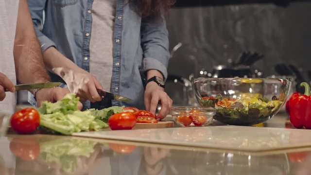 Tracking closeup shot of man and woman cutting salad and tomatoes on kitchen counter
