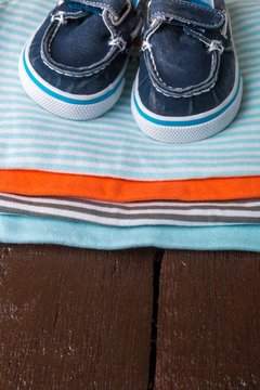 Folded blue and orange    bodysuit with boat shoes on it on  wooden background. diaper for newborn boy. Stack of infant clothing. Child outfit. Close up