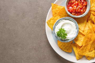 Snack for a party, chips with a tortilla, nachos with sauces: salsa with tomatoes, sour cream....