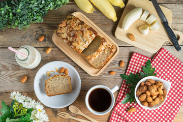 Banana cake topping with almond slice and banana, coffee, milk. Top view.