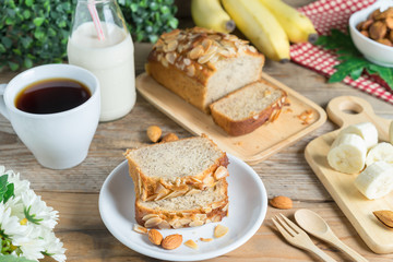 Slice of Banana cake topping with almond slice and banana, coffee, milk.