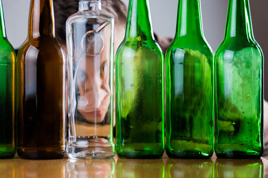 Sad young man behind green and brown glass bottles.