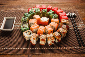 Colorful japanese sushi, food art. Appetizing colorful spiral of delicious uramaki rolls set served on brown straw mat, closeup. Oriental luxury restaurant menu photo.