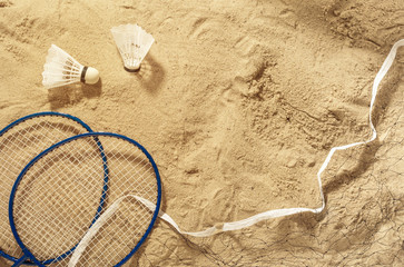 Fototapeta na wymiar Badminton rackets, net and shuttlecock on the sand, top view