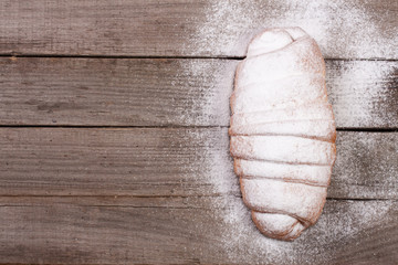 one croissant sprinkled with powdered sugar on old wooden background with copy space for your text. Top view