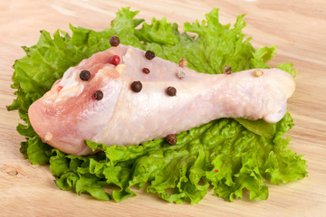 one raw chicken drumsticks with lettuce leaf on a wooden cutting board on white background