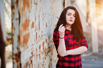 Fashion portrait girl with red lips wearing a red checkered shirt and sunglasses background rusty fence.