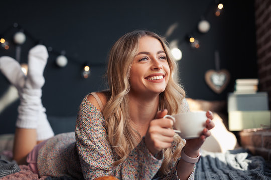 Happy woman having hot drink on bed