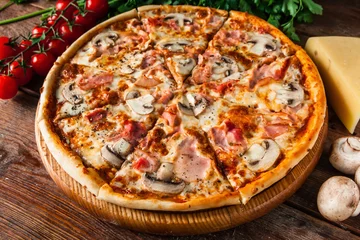 Tuinposter Pizzeria Traditionele italiaanse pizza met ham en champignons, geserveerd op rustieke houten tafel met kersen, kaas, peterselie en peperkorrels. Restaurantmenu foto.