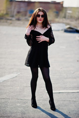 Portrait brunette girl with red lips wearing a black dress, tights and shoes on heels posed on the roof. Street fashion model.