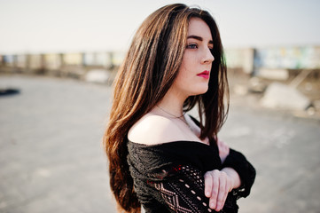 Portrait brunette girl with red lips wearing a black dress posed on the roof. Street fashion model.