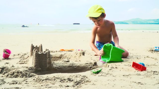 blonder bub spielt mit sand auf einem strand in thailand