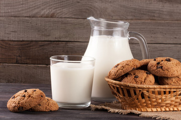 jug and glass of milk with oatmeal cookies in a wicker basket on a wooden background