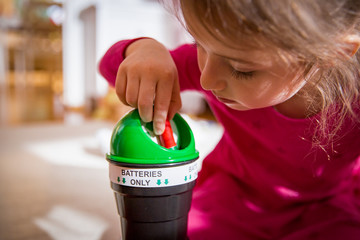 Little girl putting used batteries into recycling box at home. Child in the house room separating...
