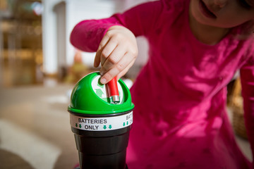 Little girl putting used batteries into recycling box at home. Child in the house room separating waste. Batteries Only.