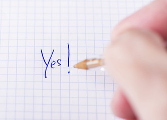Male hand writes yes on sheet of paper.
