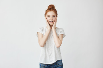 Portrait of happy redhead surprised young woman with hands on cheeks, on white background.