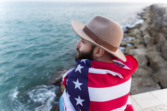 Man wrapped in American flag sitting on seashore