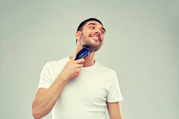smiling man shaving beard with trimmer over gray