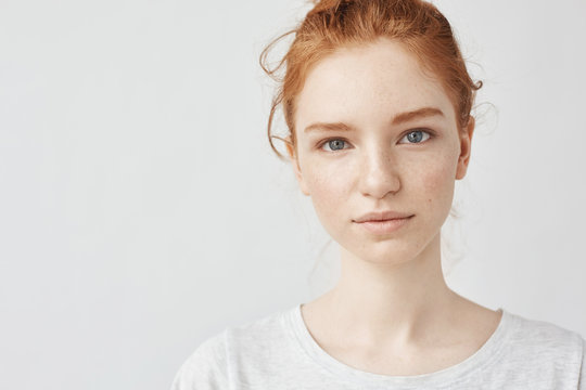 Close up portrait of young beautiful redhead girl in white shirt smiling looking at camera. Copy space. Isolated on white background.