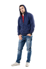 Fototapeta premium Charming man in blue hooded sweatshirt with hands in pockets looking at camera. Full body length portrait isolated over white studio background.