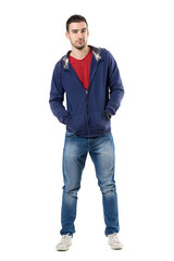 Naklejka premium Charming young guy in blue sweatshirt with hands in pockets looking at camera. Full body length portrait isolated over white studio background.