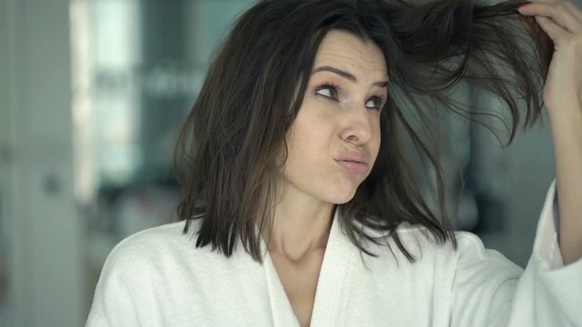 Unhappy woman on bathrobe checking her hair in mirror in bathroom 
