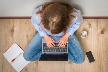 Top view of student is sitting on wood floor with laptop