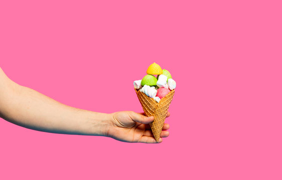 photo of female hand holding waffle cone with marshmallows on the wonderful pink studio background