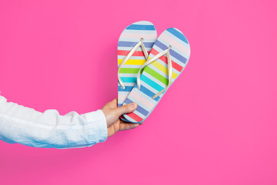 photo of male hand holding colorful sandals on the wonderful pink studio background