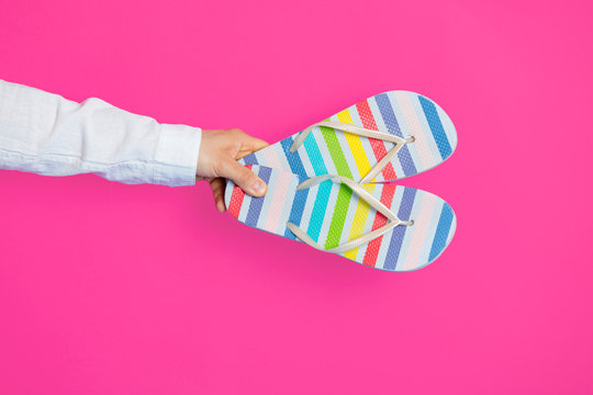 photo of male hand holding colorful sandals on the wonderful pink studio background