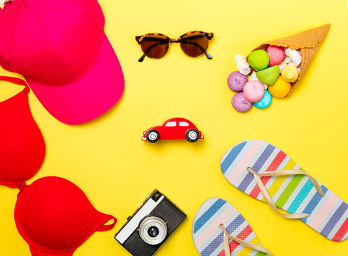 photo of swumsuit, sunglasses, hat, car shaped toy, sandals, marshmallows in waffle cone and camera on the wonderful yellow studio background