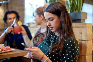 woman with smartphone and friends at restaurant