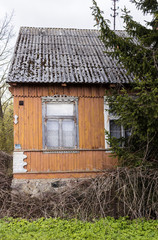 Fototapeta na wymiar An abandoned wooden house with walls painted yellow-orange paint. Window with carved clypeus. Spring in the Region Podlasie, Poland.