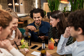 friends with drinks, credit card and bill at bar