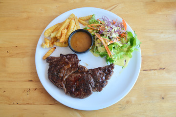 Ribeye steak with salad and French fries on wooden background