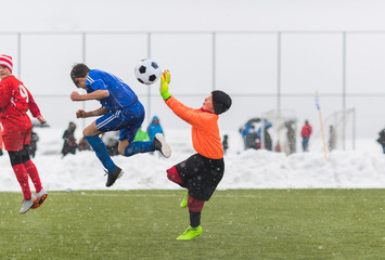 Kids soccer football tournament - children players match on soccer field during the snow falling