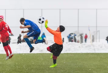 Tuinposter Kids soccer football tournament - children players match on soccer field during the snow falling © Dusan Kostic