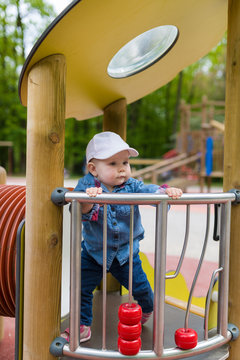 One year old baby girl standing and holding for the fence in park.