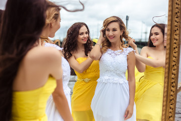 Fototapeta premium Beautiful Bride and two bridesmaids in yellow similar dresses together on a summer terrace a sea restaurant