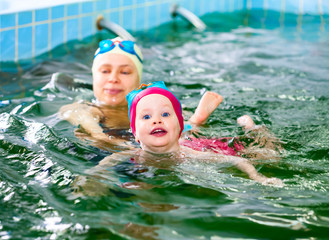 Little girl learning to swim with mother's help in a seawater swimming pool