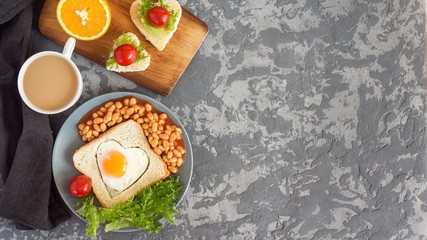 Full English Breakfast with fried eggs, beans, toasts, salad, tomatoes on gray background. Copy space