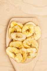 Heap of dried banana chips on wooden spoon